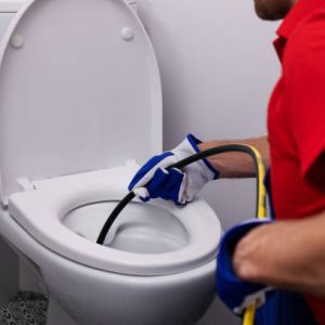 plumber unclogging blocked toilet with hydro jetting at home bathroom. sewer cleaning service