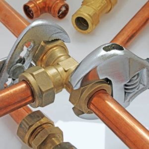 two adjustable wrenches tightening up tee-fitting on 15 mm copper pipework with loose pipe in background on white gloss surface